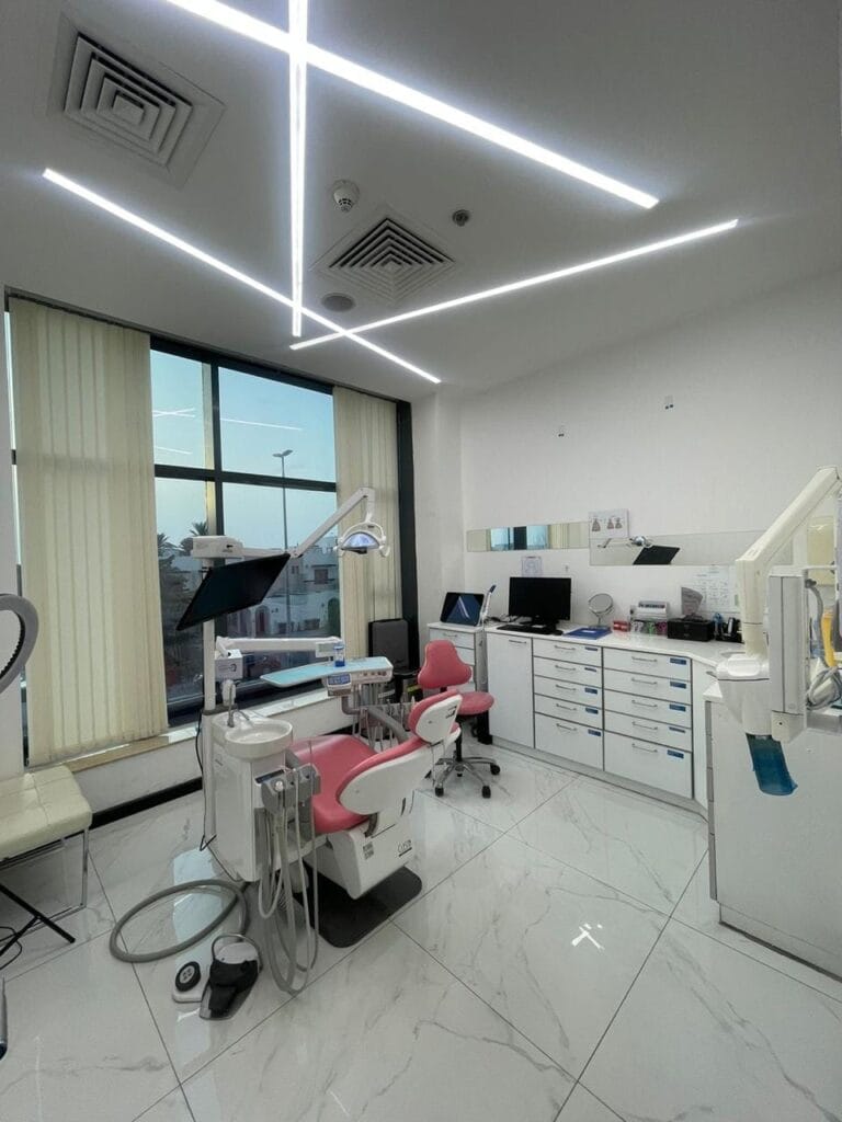 State-of-the-art dental clinic room featuring a modern pink and white dental chair, advanced equipment, floor-to-ceiling windows, and sleek cabinetry. The space is well-lit and professionally arranged, ideal for high-end patient care in Dubai.