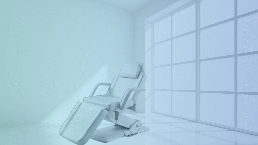 White electric treatment chair in a minimalist, bright clinic room with large window.